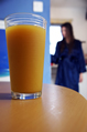 A glass of orange juice on a table with a girl in a silky blue wrapover robe in the background