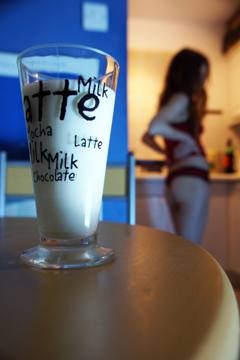 A glass of milk on a table with a girl in a vest top and knickers in the background