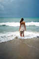 woman in white dress stands in the sea looking out to a storm on the horizon