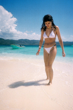 girl in white bikini walking out of turquoise sea onto white sand