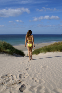 woman in yellow bikini walks through sand dunes towards beach and sea