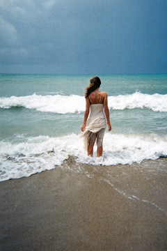 woman in white dress stands in the sea looking out to a storm on the horizon