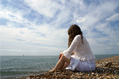 Girl in white lace sits on the waters edge loking out to sea