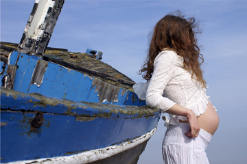 pregnant female in white lace rests against a blue boat