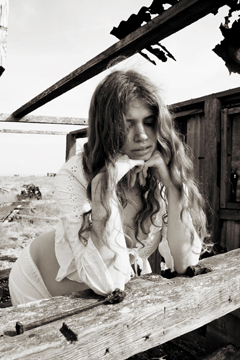 pregnant girl in white lace leans on an old wooden beam