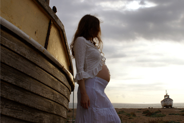 woman in white lace leans on fishing boat with second boat on the horizon