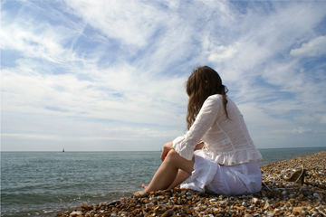 Girl in white lace sits on the waters edge loking out to sea