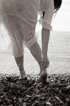 Girl in sheer white lace bends over to untie her strappy sandals