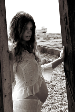 pregnant female in white lace peers into a dark shack
