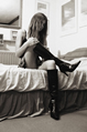Woman sitting on bed taking off knee high high-heeled boots