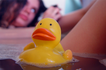 Rubber bath duck swimming past womans thigh in bath