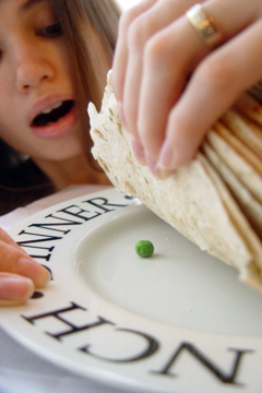 girl lifts pile of tortillas to find a pea