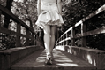 Girl in short denim skirt and sandals walks across a wooden bridge into the woods