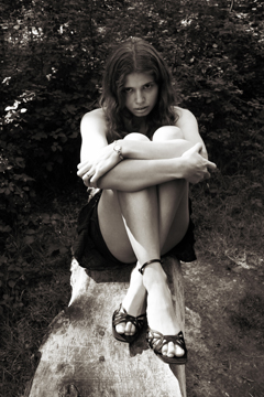 Girl in skirt and sandals sitting cross legged on a wooden bench