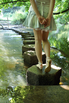 Girl in short denim skirt and sandals on stepping stones across a stream