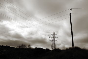 pylon power cables and telegraph wires crossing over against a stormy sky