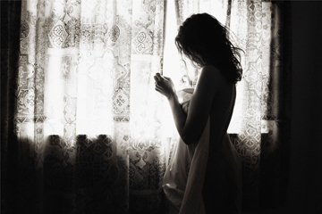 Girl wrapped in bed sheets peeking through curtains