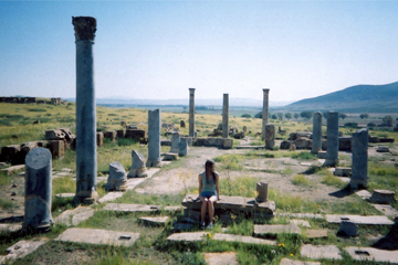 Girl sitting among ancient roman pillars in the desert